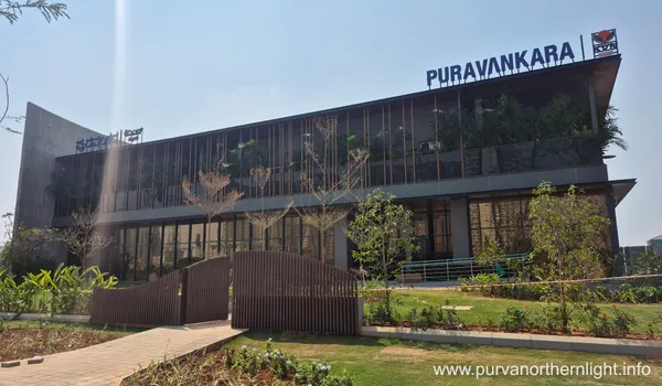 Exterior view of the Purva Northern Lights project office in Bangalore as of March 2026, featuring a two-story glass building with Puravankara signage, vertical wooden louvers, and a landscaped garden.